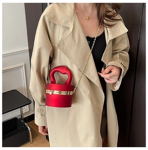 Detail of red cylindrical bucket bag with hard streamlined handle and gold chain strap