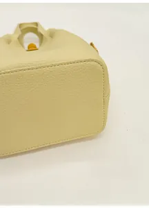 Détail du sac seau en cuir crème montrant les coutures de base et les pieds dorés