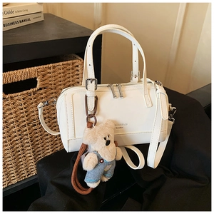 Detail of white leather boston bag featuring a fashion logo and cute plush bear charm