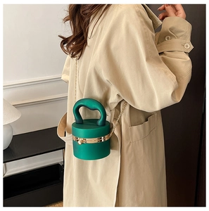 Detail of dark green cylindrical acrylic clutch bag with gold chain and metal hardware