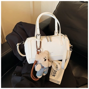 Detail view of white leather pillow bag with adjustable strap and cute teddy bear charm