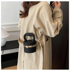 Detail of a black cylindrical crossbody bag with gold chain strap and thick handle