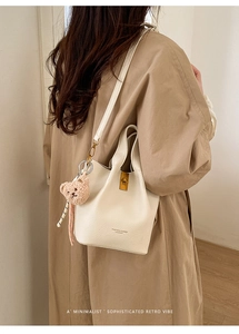 Détail du sac seau crème texture lychee avec fermoir doré et breloque ours sur mannequin