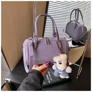 Macro detail of purple boston bag with plush bear charm reflected on a mirror