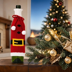 Knitted Santa wine bottle cover with white pompom and belt detail on a festive table