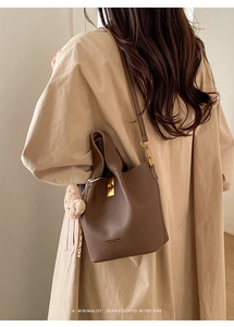 Détail d'un sac seau en cuir marron foncé avec fermoir doré sur un trench-coat