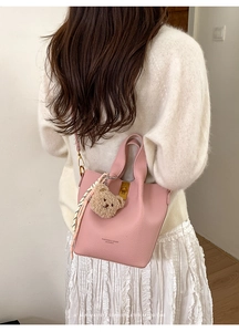Détail du sac seau en cuir rose avec breloque ours et foulard en soie sur pull blanc