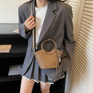 Brown leather bucket bag with round top handle and crossbody strap on a stylish model
