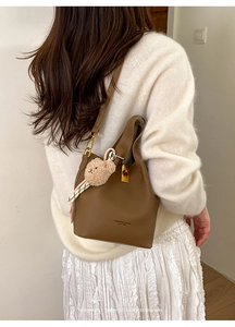 Sac seau en cuir marron avec fermoir doré et charm ours en peluche sur tenue blanche