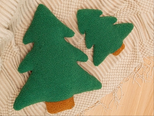 Detail of two forest green Christmas tree shaped plush pillows on a cozy knit blanket