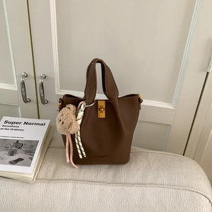 Détail du sac seau en cuir marron foncé avec fermoir doré et breloque ours en peluche