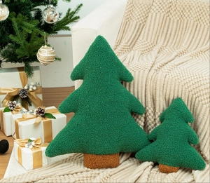 Two Christmas tree shaped plush pillows on a white sofa with warm holiday decor