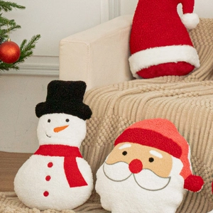 Plush Christmas themed throw pillows with snowman and Santa designs on a cozy sofa