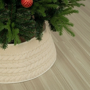 Creamy white cable knit Christmas tree collar on light wood floor with festive ornaments