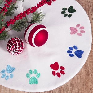 White Christmas tree skirt featuring colorful embroidered paw prints on wooden background