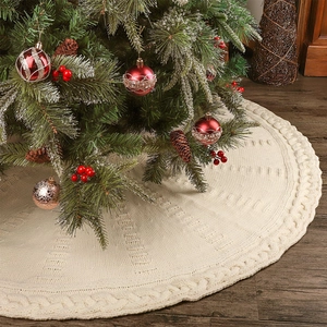 Off-white cable knit Christmas tree skirt with thick braided edges on wood floor