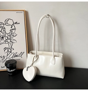Detail of a creamy white PU leather tote bag with a heart-shaped charm and logo embossment