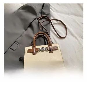Detail shot of a cream square bag with brown handle and metallic clasp on a blazer