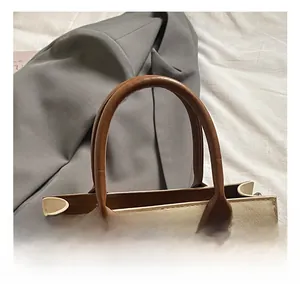 Detail of contrast stitching and brown leather handle on a chic cream handbag