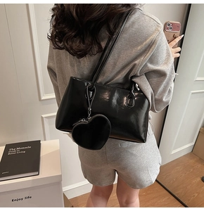 Minimalist black tote bag with heart pendant accessory shown on shoulder by model