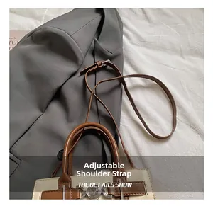 Detail of two-tone square bag with adjustable brown leather strap and metal twist lock