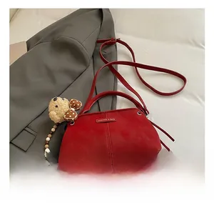 Detail of red leather crossbody bag with vertical stitching and cute bear charm accessory