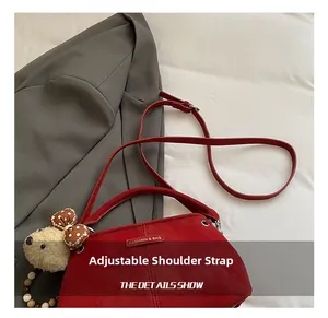 Detail of red leather crossbody bag featuring adjustable strap and plush bear charm