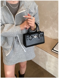 Detail of a black faux-croc handbag featuring a silver circular metal buckle on the front