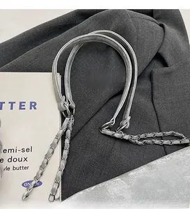 Détail d'une bandoulière en cuir gris et chaîne argentée sur blazer et livre vintage