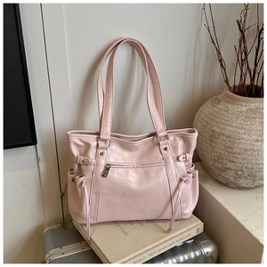 Pink faux leather tote bag with side drawstrings placed on a silver suitcase