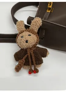 Detail of cute plush keychain with knitted sweater and earflap hat on a brown leather bag