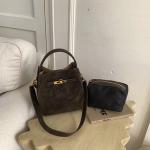 Detail of dark brown bucket bag with gold clasp and black inner canvas pouch on a table