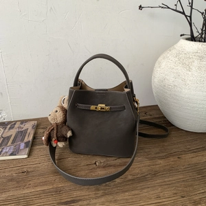 Detailed view of dark taupe bucket bag with golden twist lock and teddy bear charm
