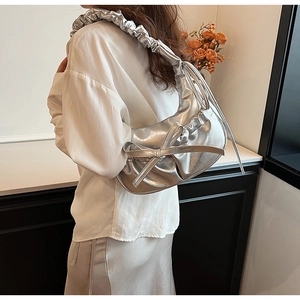 Close-up of silver bow pleated shoulder bag with metallic scrunchie strap and ribbon detail
