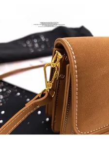 Close-up of brown pebbled leather texture with white contrast stitching and gold metal hardware