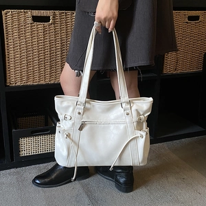 Detail of white leather tote bag featuring side drawstrings and front zipper pocket