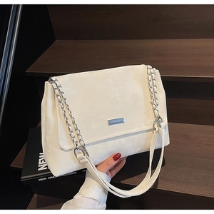 Détail d'un sac bandoulière blanc avec chaîne en métal argenté et plaque gravée élégante