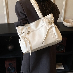 Detail of white PU leather tote bag with front pocket and drawstring on brown blazer