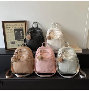 Five assorted colors of leather backpacks with fuzzy keychains and textile straps