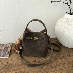 Detail of dark brown suede bucket bag with gold metal lock and plush bear charm decoration