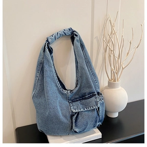 Detail of light blue denim hobo bag featuring a pleated strap and side pocket design
