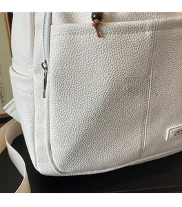 Close-up of white lychee grain leather backpack with silver zipper and wooden bead charm