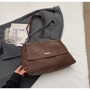 Détail du sac cabas en daim marron avec bandoulière en chaîne et plaque logo