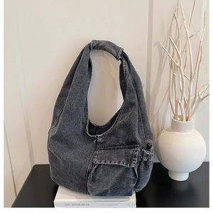 Detail of washed black denim hobo bag with front flap pocket and drawstring on white books