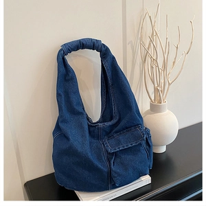 Detail of blue denim hobo bag with flap pocket and thick handle on a book shelf