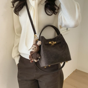 Women's brown suede bucket bag with gold clasp and cute bunny charm on white background