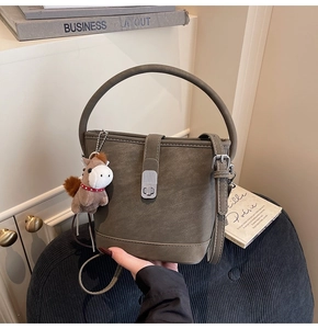 Detailweergave van een olijfgroene emmertas met litchi-textuur en een pony pluche hanger