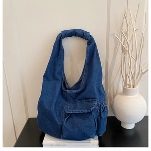 Detail of blue denim hobo bag with cloud-style pleated handle on a white book