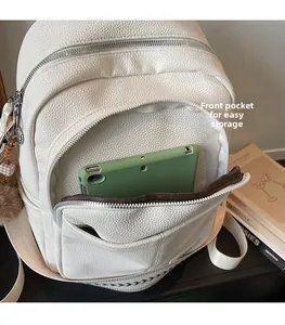 Close-up of front zipper pocket on white lychee leather backpack with plush ball charm