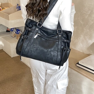 Detail of black utility tote bag showing side drawstring and multiple metal zip pockets